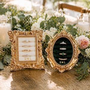 Può includere: Due cornici dorate decorate che contengono anelli. La cornice rettangolare ha un inserto in velluto color crema con quattro anelli e il testo B cuore L. La cornice ovale ha un inserto in velluto verde scuro con quattro anelli e il testo B cuore L.