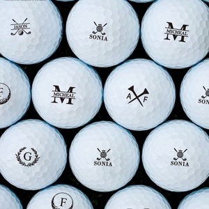May include: A close-up of ten white golf balls with black personalized text and designs. The designs include names, initials, and golf club symbols.