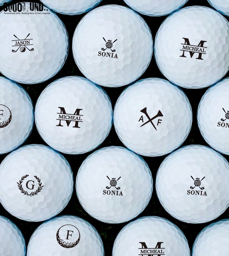 May include: A close-up of ten white golf balls with black personalized text and designs. The designs include names, initials, and golf club symbols.