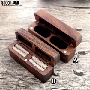 K&ouml;nnte beinhalten: Zwei h&ouml;lzerne Ringboxen, eine offen und eine geschlossen. Die ge&ouml;ffnete Box hat zwei F&auml;cher mit Ringen darin. Die geschlossene Box hat zwei F&auml;cher. Die Boxen sind aus dunklem Holz mit nat&uuml;rlicher Maserung. Die Boxen sind mit A und B beschriftet.