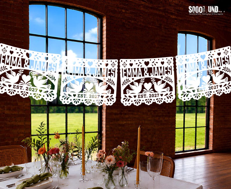 May include: A white paper banner featuring intricate cut-out designs of two doves facing each other with a heart in the center. The text "EMMA & JAMES" and "EST. 2027" is clearly visible on each panel, surrounded by decorative floral and heart patterns.