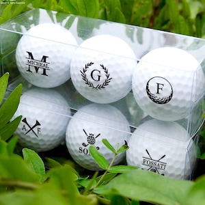 May include: Six white golf balls in a clear plastic box. Each ball has a different personalized design, including initials, names, and golf-themed graphics.