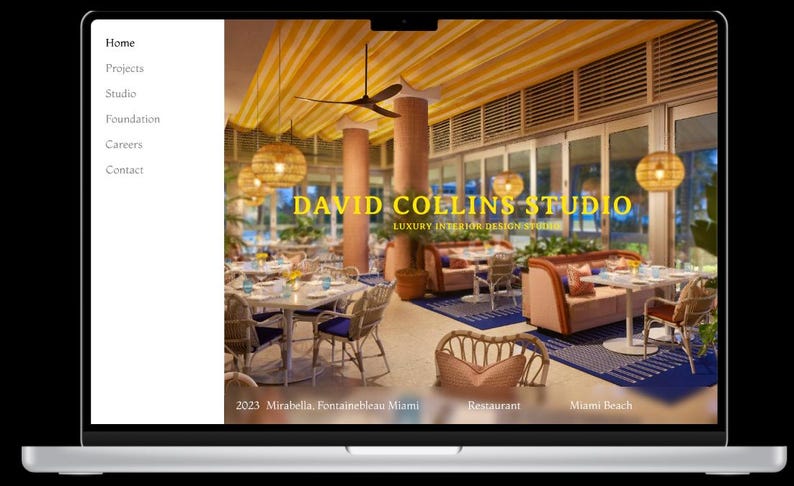 May include: A laptop computer displaying a website for David Collins Studio, a luxury interior design firm. The website features a photo of a restaurant interior with yellow striped ceilings, wicker furniture, and a blue and white patterned rug. The text "DAVID COLLINS STUDIO" is displayed in yellow on a black background.