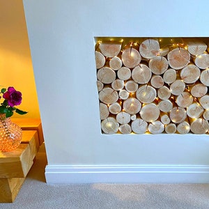 Neat round clean real wood decorative logs from The Log Basket for interior display fill a fireplace alcove stacked to show the textural growth rings or end grains with added warmth and sparkle of tiny LED fairy lights wound through the logs.