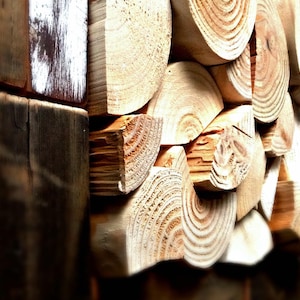May include: Close-up of a wooden wall art piece. The artwork is made from cut wood logs and planks. The wood has natural grain patterns and is in shades of brown and tan.