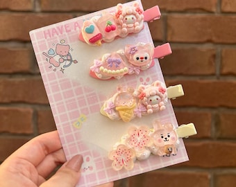 Può includere: Set di cinque mollette per capelli rosa e bianche con vari personaggi dei cartoni animati carini e disegni. Le mollette hanno uno sfondo a scacchi rosa e bianco con il testo "HAVE A" in alto.