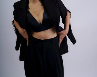 Puede incluir: Una mujer con un blazer negro con ribetes de encaje, un bralette de satén negro y pantalones negros.
