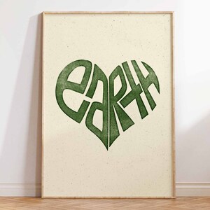 May include: A framed print with a green heart-shaped design that says "EARTH" inside. The background is a light beige with a speckled texture.