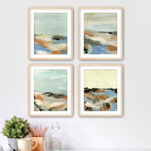 May include: Four framed abstract landscape paintings. Each artwork features a blend of colors including blue, orange, and brown, with a light blue sky. The paintings are in light wood frames, creating a cohesive set for wall decor.