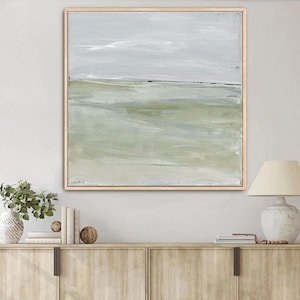 May include: A square abstract painting in a light wood frame featuring horizontal layers of muted sage green, soft gray, and white tones. The artwork displays blended brushstrokes that create a landscape-like effect with a calm, neutral color palette.