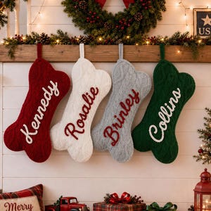 May include: Four bone-shaped Christmas stockings made of cable-knit fabric in red, white, gray, and dark green. Each stocking features a hanging loop and is personalized with embroidered names: Kennedy, Rosalie, Brinley, and Collins in script.