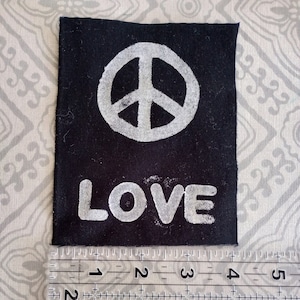 May include: Black fabric patch with a white peace symbol and the word "LOVE" printed below. The patch measures approximately 2 inches wide and 2.5 inches tall.
