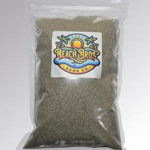 Peut inclure: Un sac en plastique transparent rempli de sable gris fin. Le sac porte une étiquette blanche avec le texte "Beach Bros Sand Co." dans un design coloré avec des palmiers, un soleil et des vagues. Le sable semble être de couleur naturelle.