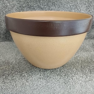 May include: A round ceramic mixing bowl featuring a smooth, light tan speckled body and a wide, dark brown band around the upper rim. The bowl has a deep, open basin with a consistent matte finish across the exterior and a slightly glossy interior.