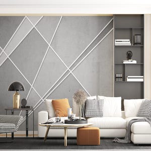 Può includere: Un divano componibile bianco con cuscini a motivi grigi e bianchi si trova in un soggiorno con una parete in cemento grigio con linee geometriche bianche. Una poltrona a motivi bianco e nero si trova in primo piano.