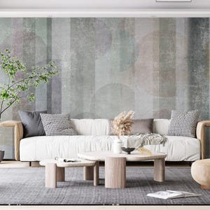May include: A white sofa with cushions sits in a living room with a patterned wall, a small tree, and a coffee table with a vase of flowers. A brown armchair sits in the corner of the room.