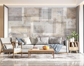 Puede incluir: Un sofá gris claro con una manta azul y almohadas, una mesa de café de madera con un tazón de fruta y una mesa auxiliar de madera con una planta y artículos decorativos. La pared detrás del sofá está decorada con una gran impresión abstracta en tonos grises y marrones.