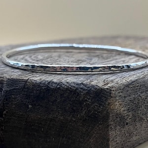 May include: A silver hammered bangle bracelet. The bracelet is smooth and shiny, with a hammered texture.