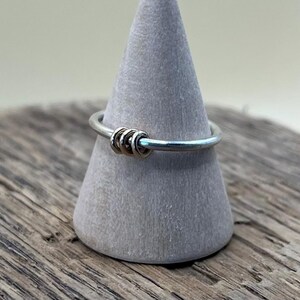 May include: A silver ring with a cluster of four gold rings in the centre.