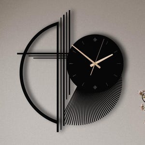 Puede incluir: Un reloj de pared negro con esfera circular y manecillas doradas, montado sobre un marco decorativo compuesto por un semicírculo, líneas verticales y un abanico de finas láminas negras que se extienden desde la parte inferior derecha.