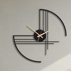 Può includere: Un orologio da parete moderno in metallo nero con un design minimalista. L'orologio presenta un quadrante circolare con lancette beige e una cornice geometrica astratta. È montato su una parete chiara, con una sedia e un tavolo in primo piano.