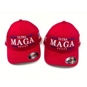 May include: Two red baseball caps with white embroidered text that reads "Ultra MAGA" with five stars below the text. The caps have a blue and white American flag on the side.
