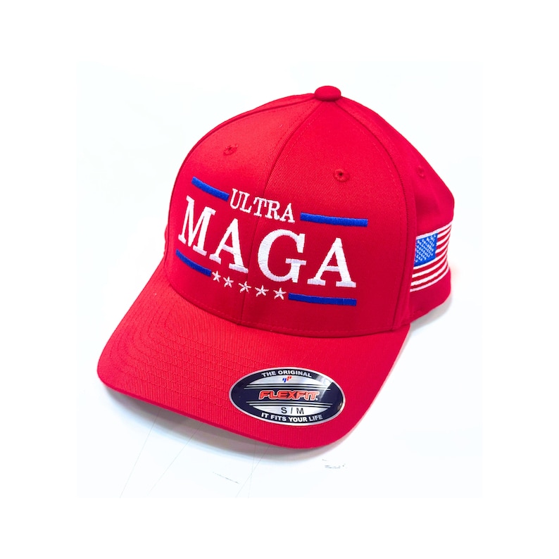 May include: Red baseball cap with the text "ULTRA MAGA" in white with blue accents and four stars. The cap has a small American flag on the side and a "Flexfit" label on the bottom.