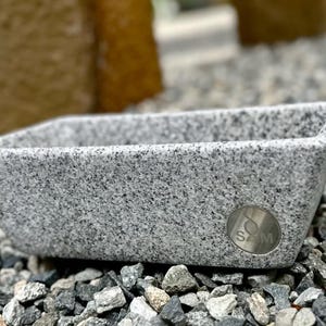 May include: A gray granite rectangular planter with a silver metal label that says "SM".