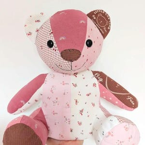 May include: A patchwork teddy bear constructed from various fabrics in shades of pink, white, and brown. The bear features floral, cherry, and rainbow patterns, black button eyes, a brown nose, and text on the ear and arm reading Little Cub Club.
