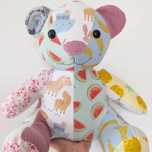 May include: A patchwork teddy bear constructed from various patterned fabrics featuring illustrations of watermelons, bananas, zebras, and boats. The bear has black button eyes, a pink stitched nose, and the name Annie and date 20.12 embroidered.