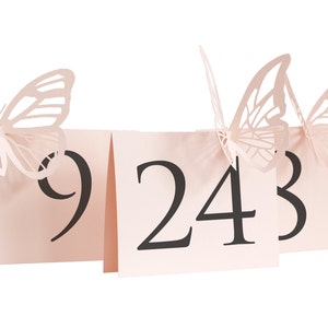 Op de afbeelding: Drie roze papieren tafelnummerkaarten met vlinderuitsnijdingen. De nummers 9, 24 en 3 zijn in zwart op de kaarten gedrukt.