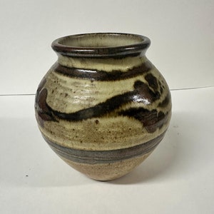 Puede incluir: Un jarrón de cerámica marrón y crema con un diseño pintado a mano. El jarrón tiene un cuerpo redondeado y una abertura ancha.