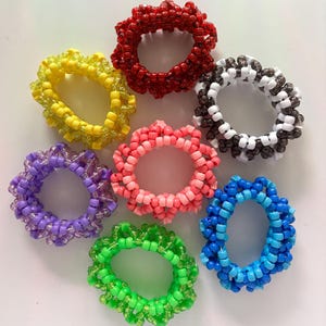 Puede incluir: Siete gomas para el pelo de cuentas de colores en varios colores, incluyendo rojo, amarillo, rosa, morado, blanco, negro y azul.