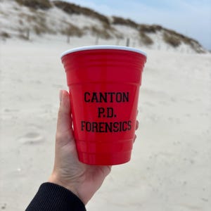 Puede incluir: Un vaso de plástico rojo con un borde blanco. El vaso tiene texto negro que dice "CANTON P.D. FORENSICS".
