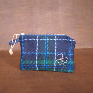 以下が含まれることがあります： 金色の刺繍が施されたクローバーがついた、青と緑の格子柄の小さなジッパー付きポーチ