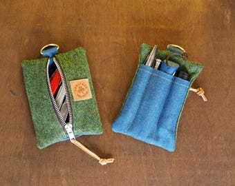 May include: Two small green fabric pouches with gold-coloured rings. One is open, revealing cards, and the other has blue denim pockets holding pens and a small torch. Both have leather tags.