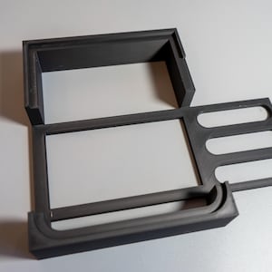 Könnte beinhalten: Ein schwarzer Plastik-Organizer mit mehreren Fächern. Der Organizer hat eine rechteckige Form mit einer erhöhten Lippe an der Vorderkante. Die Fächer sind für die Aufbewahrung von kleinen Gegenständen wie Stiften, Bleistiften oder anderen Büroartikeln konzipiert.