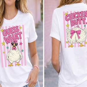 May include: White t-shirt with a humorous design. The front features the text "GUESS WHAT" above a cartoon chicken wearing sunglasses. The back displays "CHICKEN BUTT" above a chicken with a pink bow. Pink and white striped background.