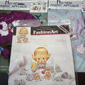 May include: A white t-shirt with an iron-on design of an angel holding a baby chick. The angel is surrounded by Easter eggs. The design is from FashionArt and is titled "Gifts of Easter by Ruth J. Morehead".