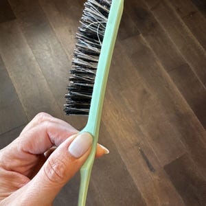 May include: A light green hair brush with black bristles. The brush is held in a hand.