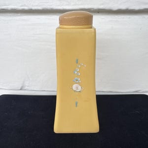 May include: A yellow ceramic bottle with a wooden lid and floral design. The bottle has a floral design with blue and white flowers.