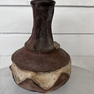 May include: A brown and white ceramic vase with a unique, textured design. The vase has a wide base and a narrow neck.