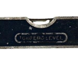 May include: A dark blue metal torpedo level tool featuring three clear liquid-filled vials for horizontal, vertical, and 45-degree angle measurements. The tool has a silver-colored frame and the text TORPEDO LEVEL embossed on the front surface.
