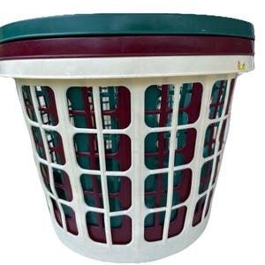 以下が含まれることがあります： 白いプラスチック製のランドリーバスケット。格子模様で、濃い緑色の蓋とバーガンディ色の縁が付いています。バスケットの内側はティールとバーガンディです。