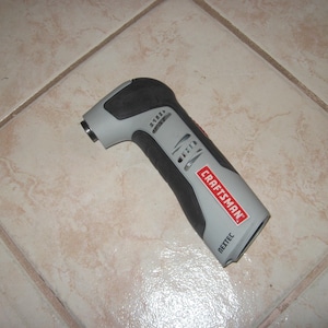May include: A Craftsman Nextec cordless multi-tool in gray and black, with the Craftsman logo in red. The tool is angled and has a textured grip. It is lying on a light-colored tiled surface.