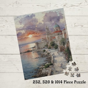 May include: A partially assembled jigsaw puzzle featuring a coastal town scene at sunset. The puzzle depicts buildings with red-tiled roofs, a domed structure, and a waterfront promenade. The text "252, 520 & 1014 Piece Puzzle" is at the bottom.