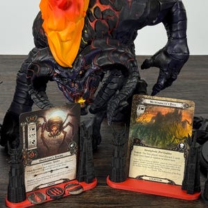 May include: A collection of Lord of the Rings figurines and game cards. The figurines include a black armored figure, a fiery Balrog, and Gandalf. The game cards are displayed in black and red card holders.