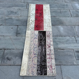 May include: A long, narrow rug made from recycled fabric scraps. The rug has a patchwork design with different colors and patterns, including red, white, black, and brown.