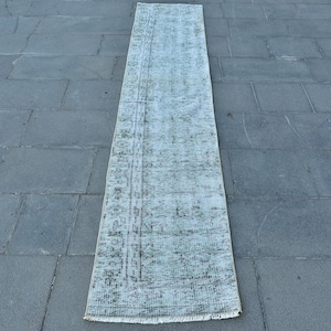 Pode incluir: Um tapete corredor vintage branco e verde com um padrão floral. O tapete tem uma borda franjada e está colocado sobre um piso de ladrilhos cinzentos.