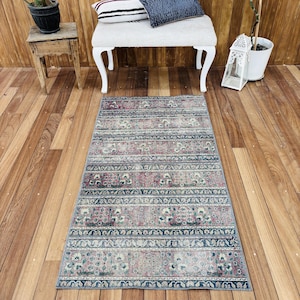 May include: A rectangular area rug featuring a repeating pattern of horizontal bands in muted shades of pink, blue, and cream. The design includes intricate floral motifs and geometric borders that span the entire length of the textile floor covering.